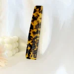 Tortoiseshell cellulose acetate comb with fine and wide teeth on a light display background