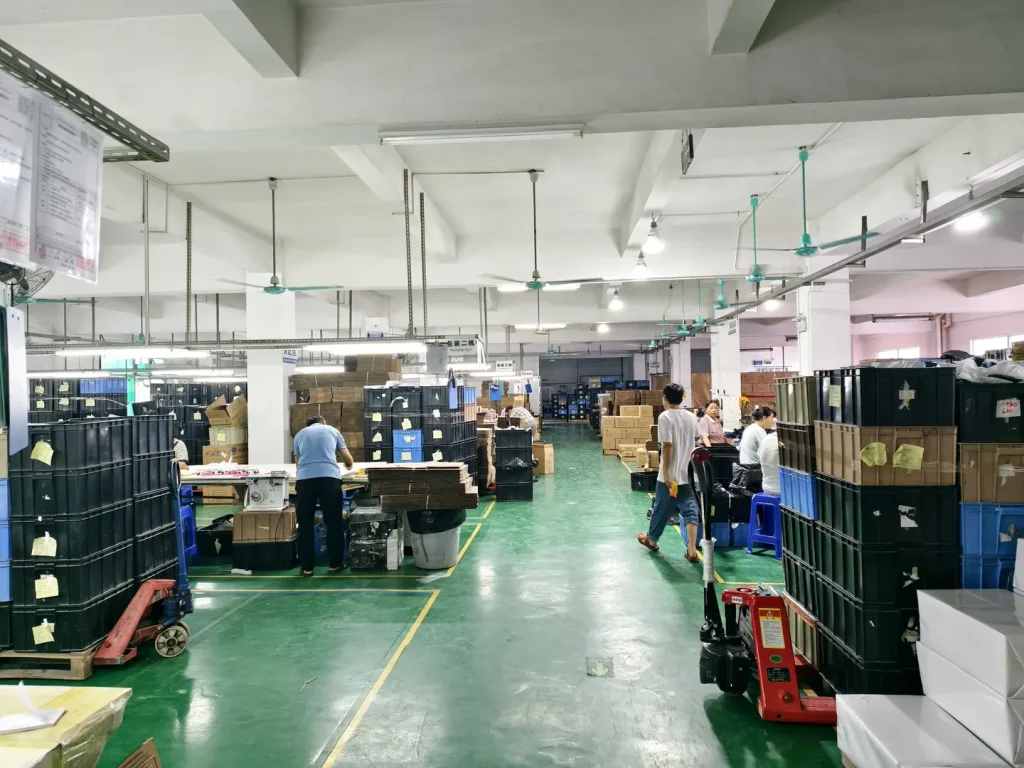 Workers and stacked production bins across a hairbrush workshop with marked green aisles.
