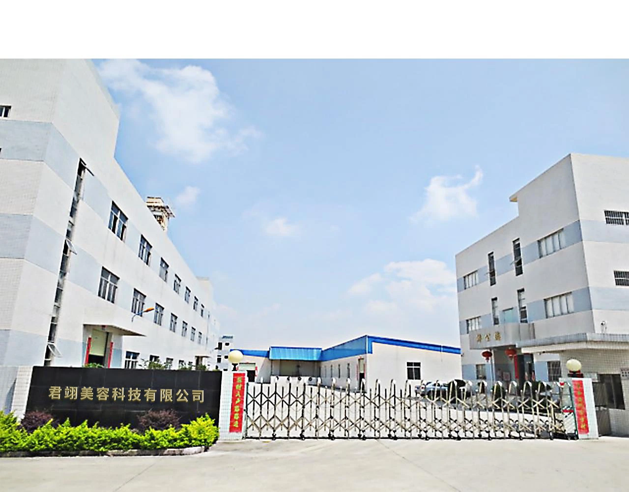 Factory entrance with a retractable gate and white multistory buildings.