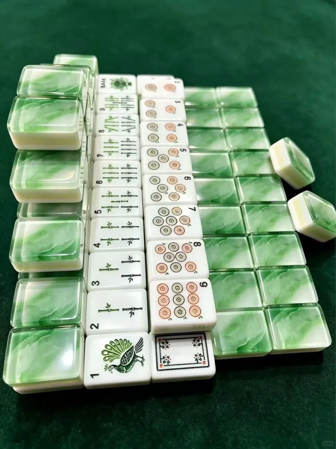 Mahjong tiles with green translucent patterned backs arranged beside printed tile suits