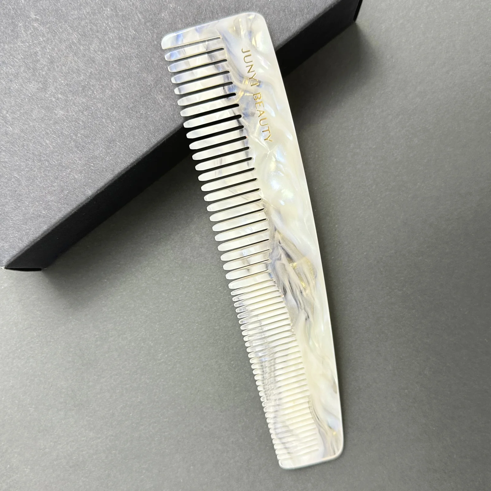 Pearl ivory cellulose acetate comb with fine and wide teeth on a dark display background